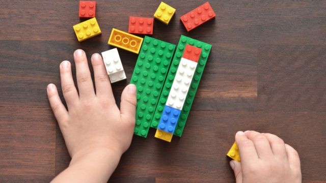 A close up of a child's hands playing with colorful Lego blocks on a wooden table