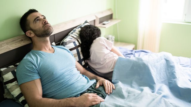 A man and woman sitting in bed during the coronavirus lockdown with the man showing an exasperated look on his face as the woman turns away.