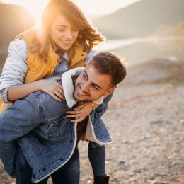 A young woman jumps on her boyfriends back on a lakeshore in autumn.