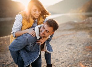 A young woman jumps on her boyfriends back on a lakeshore in autumn.