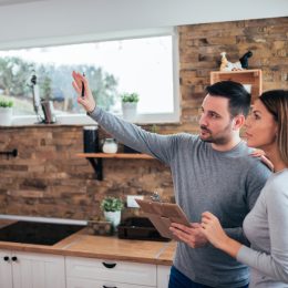 A young couple standing in their kitchen holding a clipboard and planning amazing home upgrades