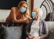 Senior woman in medical mask with social worker visiting her at home