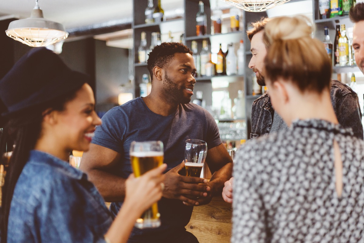 group of happy friends meeting in a pub, standing by the bar counter talking and drinking beer