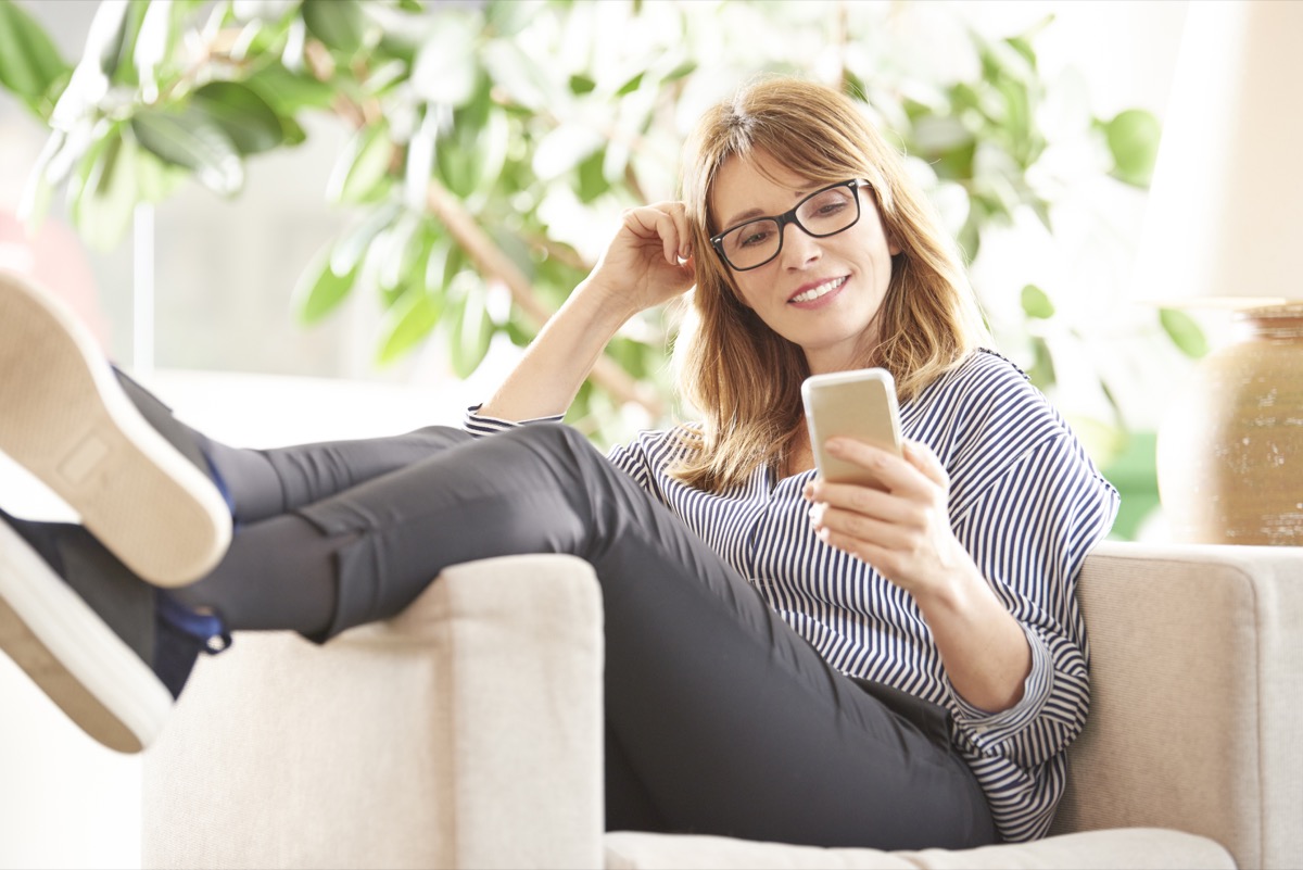 Woman sitting sideways in chair with her feet up, scrolling phone and smiling