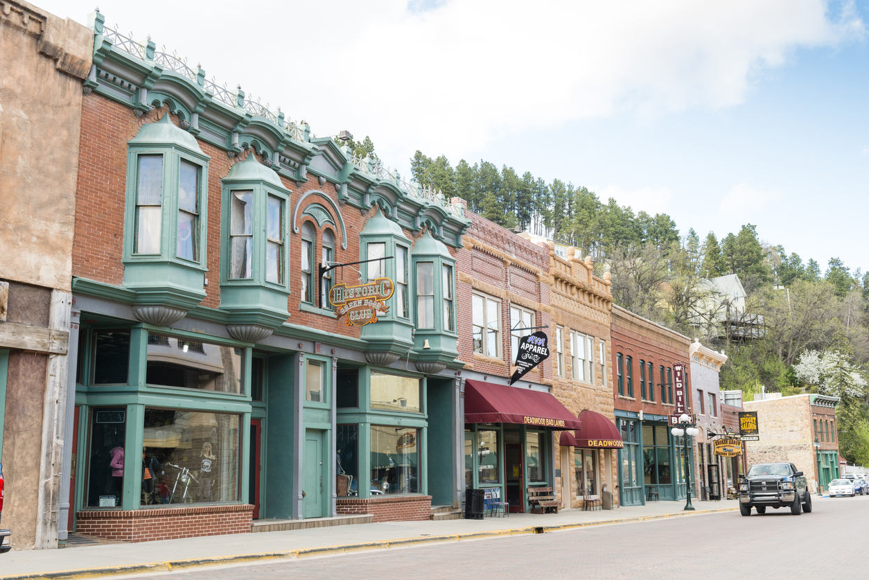The main street of Deadwood, South Dakota lined with shops and a passing vehicle.