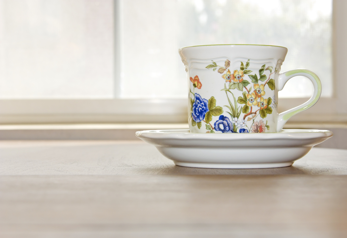 fancy floral tea cup sitting on wood table beneath window