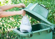 hand throwing away bag of trash in large outdoor bin