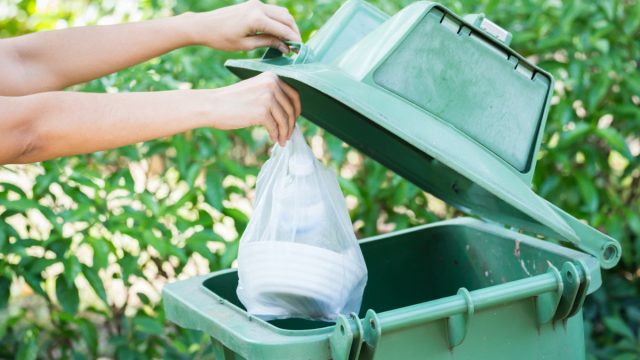 hand throwing away bag of trash in large outdoor bin
