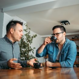 Two casual businessmen talking and drinking coffee at workplace