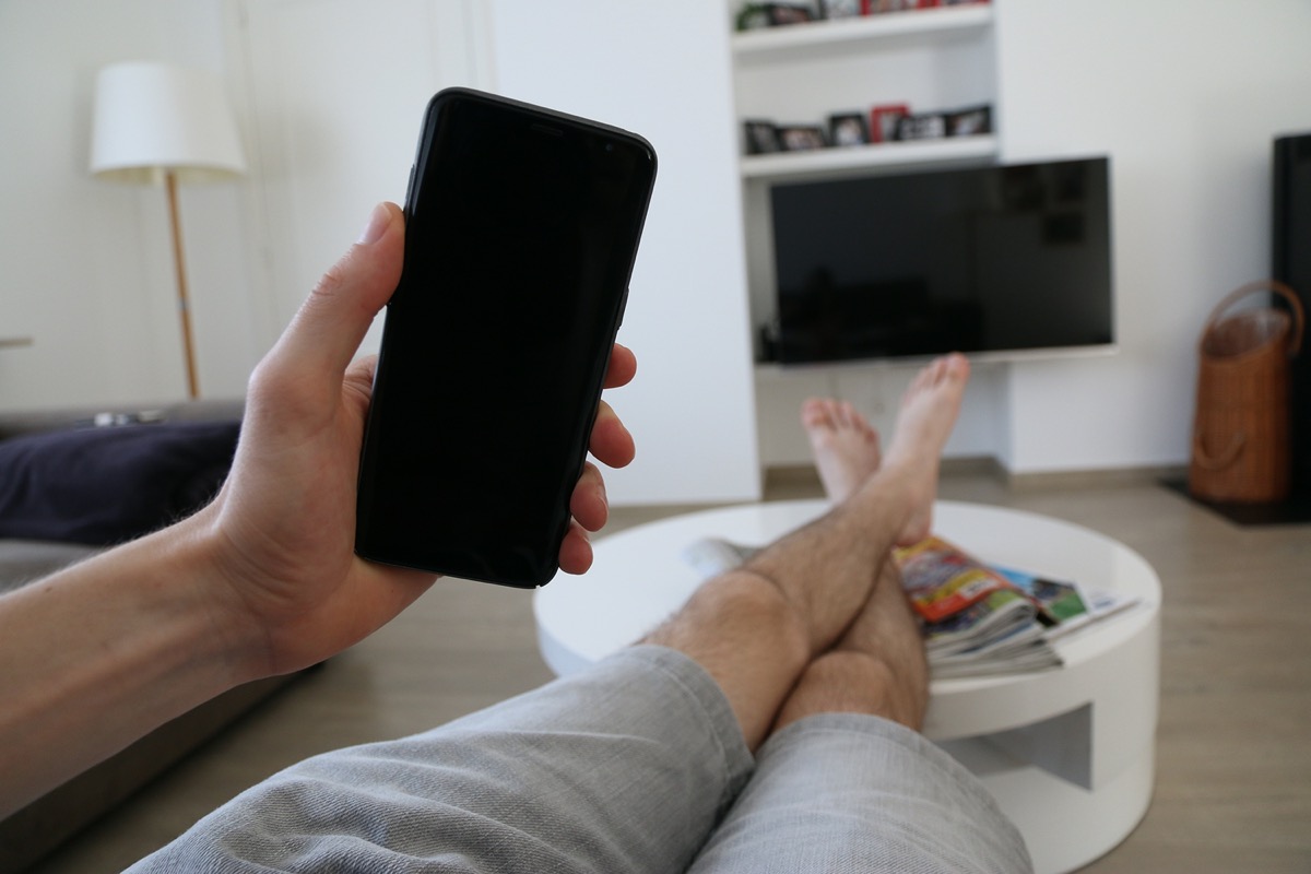 white man holding smartphone watching tv