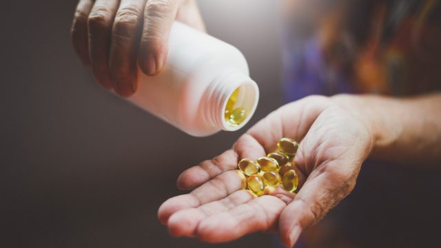 A man pouring out vitamin capsules from a white bottle into his hand.