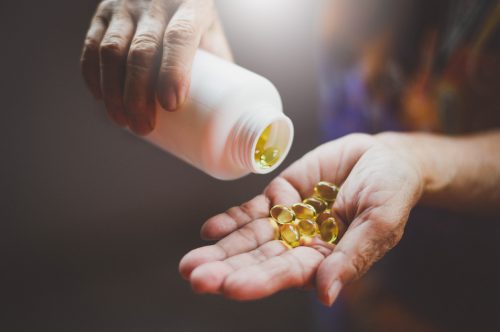 A man pouring vitamin capsules from a white bottle into his hand.