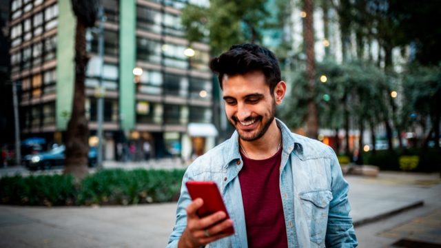 Portrait of a handsome smiling man using mobile phone at the street.