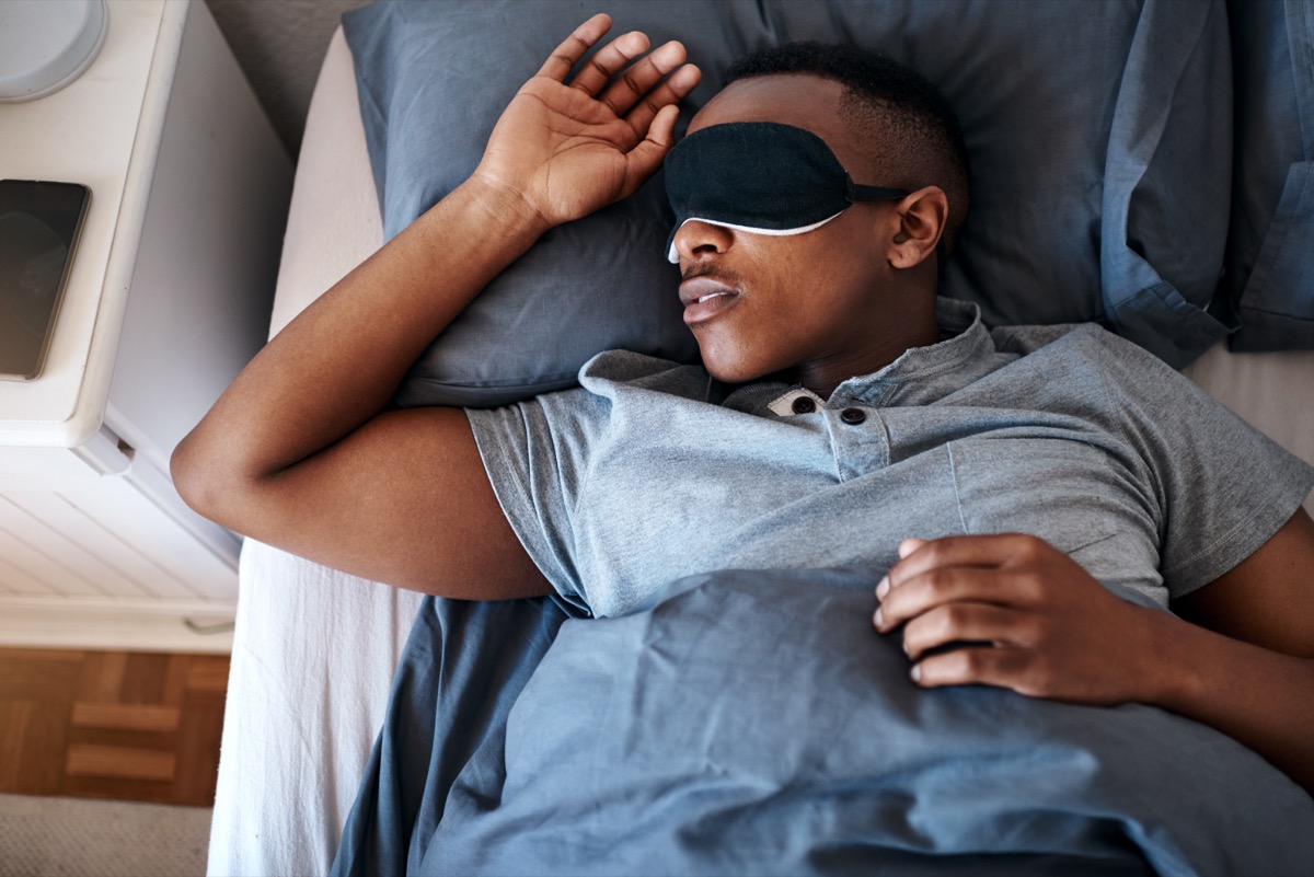 Young man wearing a night mask and sleeping in his bed at home
