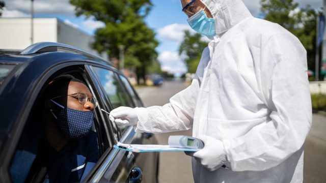 Doctor in a protective suit taking a nasal swab from a person to test for possible corona virus infection on the street. Diver through covid-19 testing center in city.