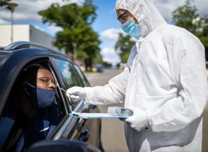 Doctor in a protective suit taking a nasal swab from a person to test for possible corona virus infection on the street. Diver through covid-19 testing center in city.
