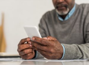 cropped view of senior man using smartphone while sitting at table