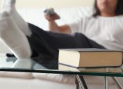 A man sitting with his feet on top of a glass coffee table next to a book.