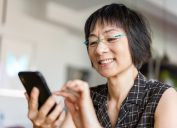 Senior Asian woman laughing when using a smartphone.