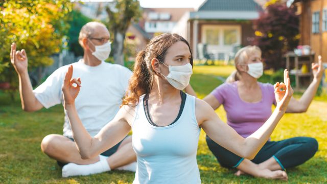 A group of mixed aged people do yoga outdoors with face masks on to stop the spread of COVID