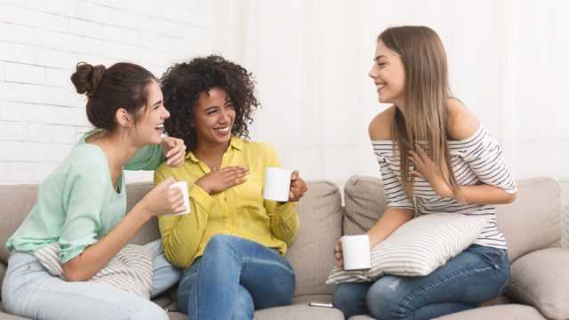 three young women talking and drinking tea on the couch