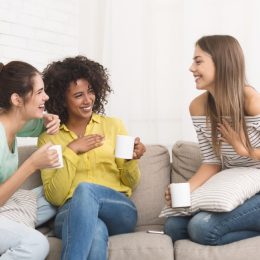 three young women talking and drinking tea on the couch