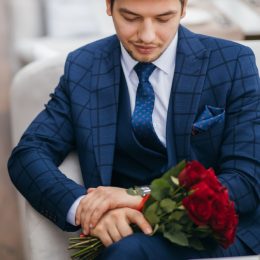 man in suit holding flowers and looking at watch