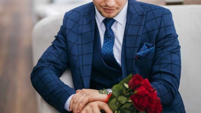 man in suit holding flowers and looking at watch