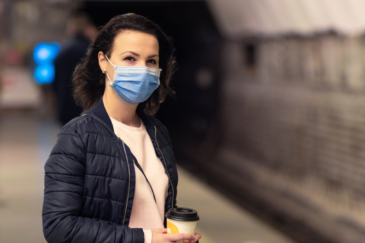 woman with a face mask and a coffee waiting for the train