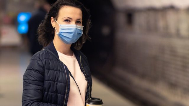 woman with a face mask and a coffee waiting for the train