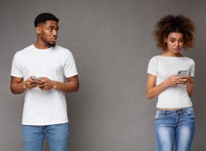 Sad man looking at his girlfriend, who is texting on phone, on gray background