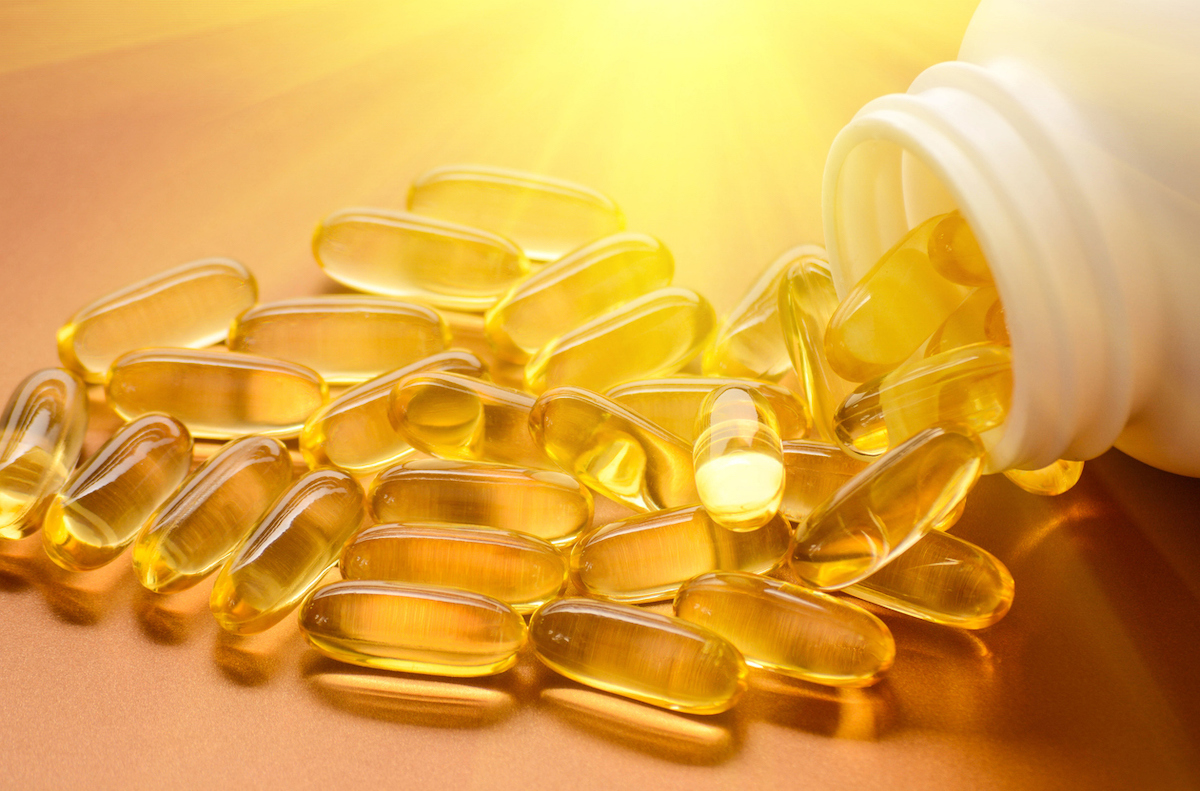 close up of vitamin d capsules spilling out of bottle with sunshine lighting them up