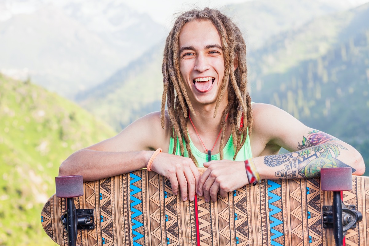 young white guy with dreadlocks sticking tongue out and holding skateboard