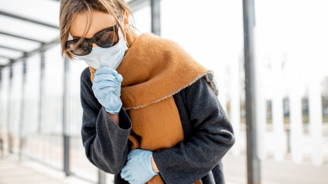 Woman in face mask coughing outdoors