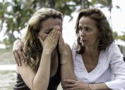 middle aged white woman comforts friend who is dealing with a loss, her head is in her hands