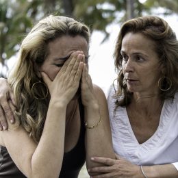 middle aged white woman comforts friend who is dealing with a loss, her head is in her hands