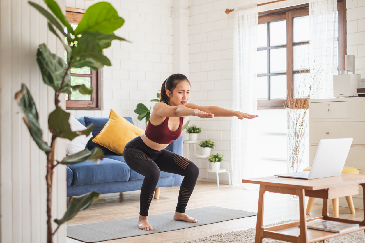 A young woman doing yoga in her living room in front of her laptop.