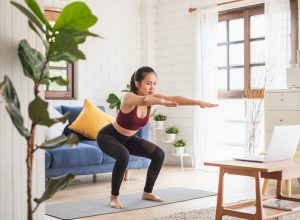 A young woman doing yoga in her living room in front of her laptop.
