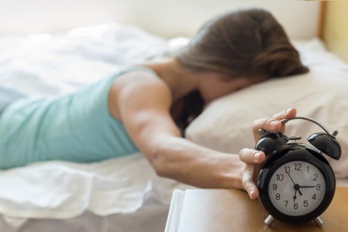 A tired woman in bed hits her alarm clock to stop it from going off.