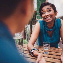Young woman sitting in stylish cafe apologizing, gesturing and searching for an excuse to tell her boyfriend