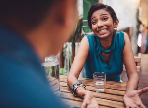 Young woman sitting in stylish cafe apologizing, gesturing and searching for an excuse to tell her boyfriend