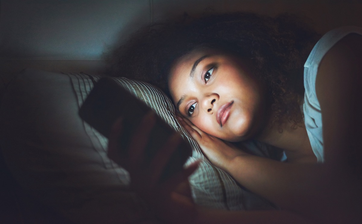 Shot of a young woman using a cellphone in bed at night
