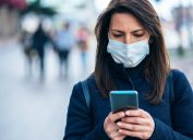 A young woman using her smartphone while wearing a mask due to the coronavirus pandemic.