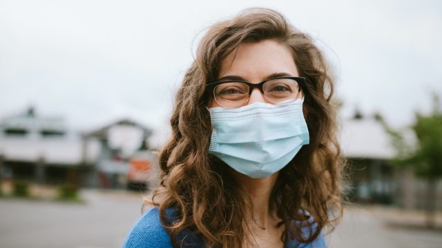 A young woman smiles while wearing a face mask and eyeglasses.