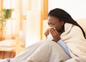 young black woman under blanket sneezing or blowing nose while sick
