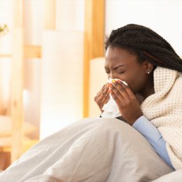 young black woman under blanket sneezing or blowing nose while sick