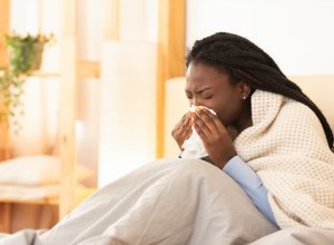 young black woman under blanket sneezing or blowing nose while sick