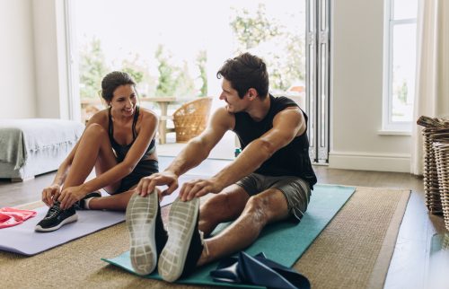 Cuplu tânăr care practică împreună pe covorașe de yoga în camera de zi.