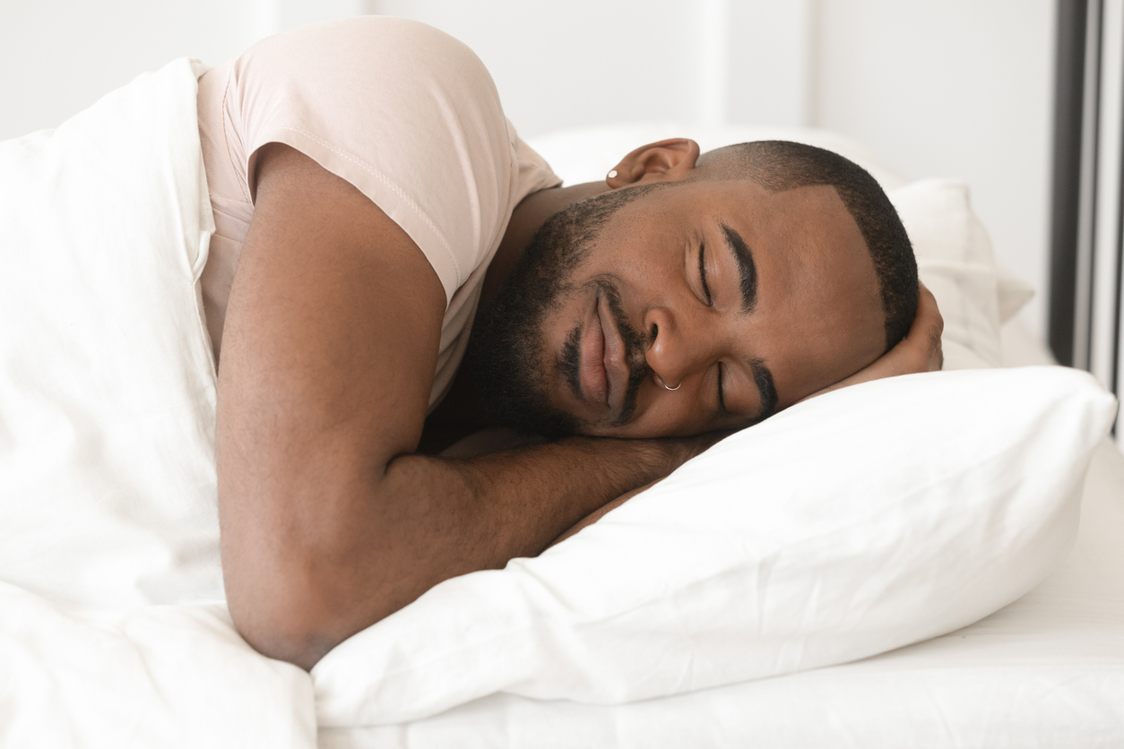 A young Black man sleeping comfortably in bed.