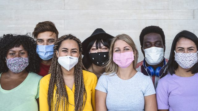 A group of multiethnic young people wearing different face masks and smiling.